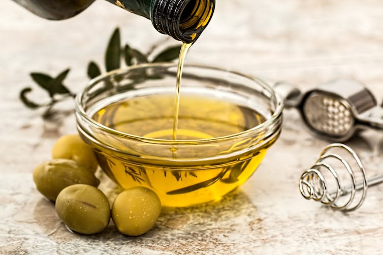 olive oil pouring into a glass dish, with some green olives