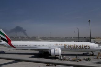 A plume of smoke caused by an Iranian strike is seen in the background as an Emirates plane is parked at the Dubai International Airport. (AP Photo)