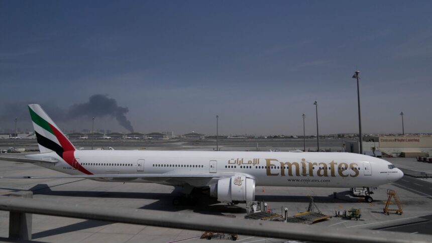 A plume of smoke caused by an Iranian strike is seen in the background as an Emirates plane is parked at the Dubai International Airport. (AP Photo)