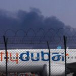 A FlyDubai plane is parked at Dubai International Airport as smoke rises in the background after a drone struck a fuel tank early morning, forcing the temporary suspension of flights, in Dubai. (AP Photo)