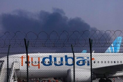 A FlyDubai plane is parked at Dubai International Airport as smoke rises in the background after a drone struck a fuel tank early morning, forcing the temporary suspension of flights, in Dubai. (AP Photo)