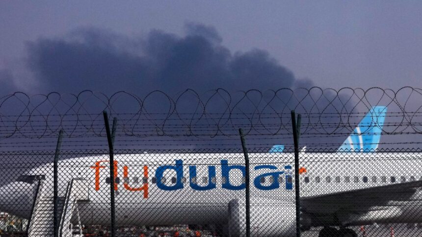 A FlyDubai plane is parked at Dubai International Airport as smoke rises in the background after a drone struck a fuel tank early morning, forcing the temporary suspension of flights, in Dubai. (AP Photo)
