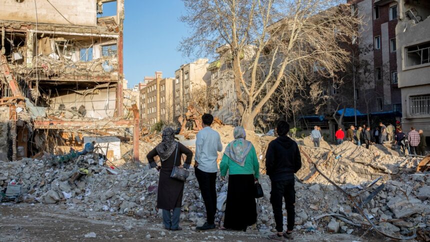 People walk through an area hit by airstrikes in Tehran, Iran