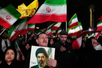 Pro-government supporters wave national flags as one of them holds a picture of the Supreme Leader Ayatollah Mojtaba Khamenei during a rally in a square in western Tehran, Iran. (AP Photo)