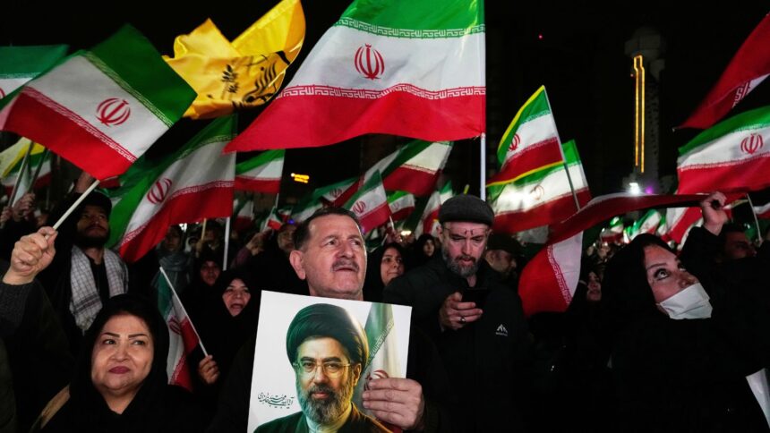 Pro-government supporters wave national flags as one of them holds a picture of the Supreme Leader Ayatollah Mojtaba Khamenei during a rally in a square in western Tehran, Iran. (AP Photo)