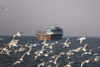 FILE PHOTO: Birds fly near a boat in the Strait of Hormuz amid the U.S.-Israeli conflict with Iran, as seen from Musandam, Oman, March 2, 2026. | REUTERS/Amr Alfiky/File Photo