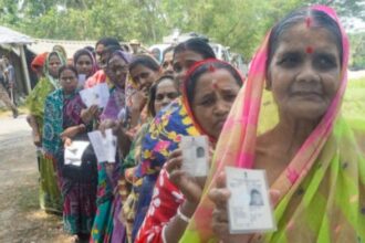 Voters show their voting cards while waiting in line to cast their votes during the first phase of the West Bengal Assembly elections 2026 at a polling station, in Purba Medinipur on Thursday. (ANI Photo)