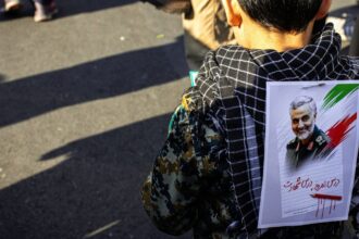 AN Iranian child with a poster of slain military leader Qassem Soleimani pinned to his back during the 2020 Iran-US conflict (Unsplash@hoseinchaharbaghi).
