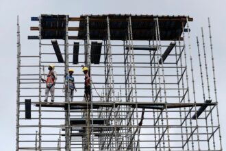 Migrant construction workers on a scaffold in Kerala, as large-scale return migration for elections in West Bengal and Assam disrupts key labour-dependent industries.