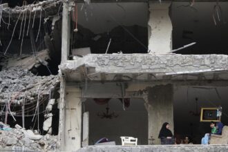 The wife and children of Fadi Al Zein, who lost both his homes in Israeli strikes in his village of Khiam and in Dahiyeh, sit on the balcony of their heavily damaged apartment building in Beirut's southern suburbs