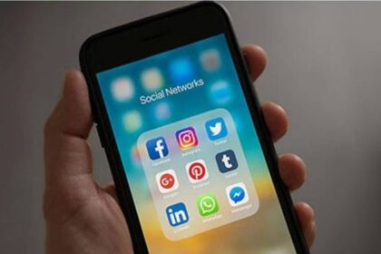 A hand holding a phone that displays social media apps such as Facebook, Instagram, X, and WhatsApp