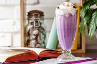 A tall glass of a purple drink topped with white ice cream.