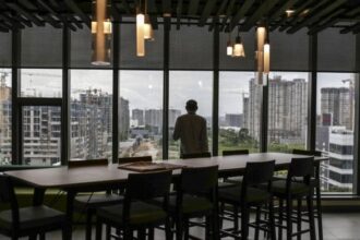 An employee standing at the window looks out over construction sites from the Amazon.com Inc. office campus in Hyderabad