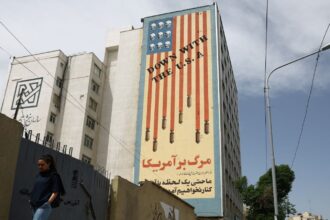 A woman walks past an anti-US mural on a building in Tehran, Iran. (REUTERS)