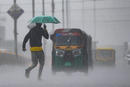 A man carrying an umbrella crosses a road amid rainfall, in Chikkamagaluru, Karnataka. (PTI Photo)