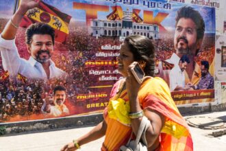 A woman walks past a banner of actor and Tamilaga Vettri Kazhagam (TVK) President Chandrasekaran Joseph Vijay, after his party surprisingly emerged as the single largest party in the April 23 polls to the Tamil Nadu state Assembly. (PTI Photo)