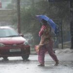 A woman crosses street through a dust storm accompanied by rain in Jammu