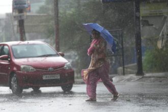 A woman crosses street through a dust storm accompanied by rain in Jammu