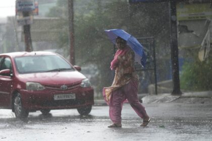 A woman crosses street through a dust storm accompanied by rain in Jammu