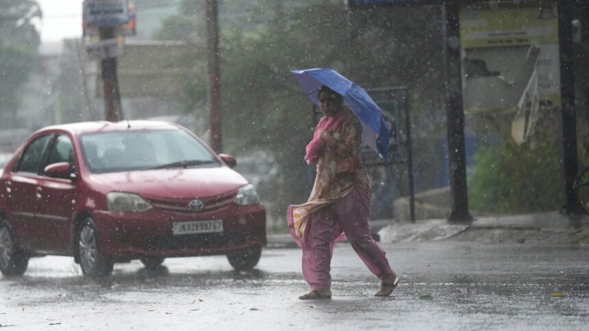 A woman crosses street through a dust storm accompanied by rain in Jammu