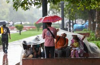 People cover their heads with a plastic sheet amid rain at India Gate lawn, in New Delhi on Saturday.