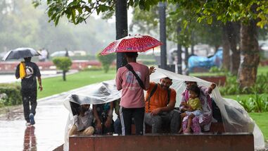 People cover their heads with a plastic sheet amid rain at India Gate lawn, in New Delhi on Saturday.