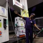 FILE PHOTO: A worker fills a car with petrol as he gestures towards the fuel barometer for the passenger to check, at a fuel station in Kolkata.