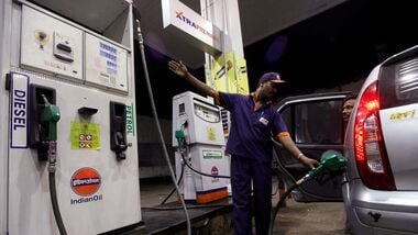 FILE PHOTO: A worker fills a car with petrol as he gestures towards the fuel barometer for the passenger to check, at a fuel station in Kolkata.