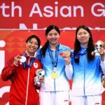 Silver medallist Japan's Satomi Suzuki (L), gold medallist China's Tang Qianting (C) and bronze medallist China's Yang Chang (R) celebrate on the podium of the women's 50m breaststroke swimming event during the 2026 Asian Games at the Tokyo Aquatics Centre in Tokyo.