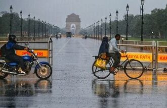 Commuters make their way through a rain-slicked road following heavy rainfall near India Gate, in New Delhi.