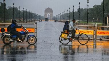 Commuters make their way through a rain-slicked road following heavy rainfall near India Gate, in New Delhi.