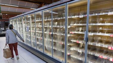 A woman walks past empty fresh-food refrigerators.