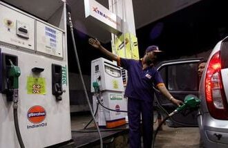 FILE PHOTO: A worker fills a car with petrol as he gestures towards the fuel barometer for the passenger to check, at a fuel station in Kolkata.