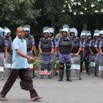 A man walks past members of the Rapid Action Force (RAF) standing guard ahead of a protest planned by the Cockroach Janta Party (CJP) seeking the resignation of India's Chief Election Commissioner Gyanesh Kumar, near the protest site in New Delhi