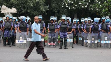 A man walks past members of the Rapid Action Force (RAF) standing guard ahead of a protest planned by the Cockroach Janta Party (CJP) seeking the resignation of India's Chief Election Commissioner Gyanesh Kumar, near the protest site in New Delhi