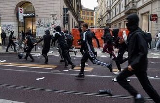 Protesters run along a street strewn with debris during a protest over the state of public services and the rising cost of living in Milan, Italy, October 18, 2026. REUTERS/Stringer