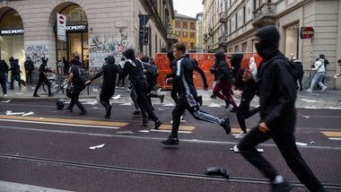 Protesters run along a street strewn with debris during a protest over the state of public services and the rising cost of living in Milan, Italy, October 18, 2026. REUTERS/Stringer
