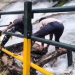 Forest department personnel clean safety railings clogged with debris amid swollen waters at Kumbakkarai Falls near Periyakulam, in Theni district, Tamil Nadu