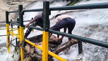 Forest department personnel clean safety railings clogged with debris amid swollen waters at Kumbakkarai Falls near Periyakulam, in Theni district, Tamil Nadu